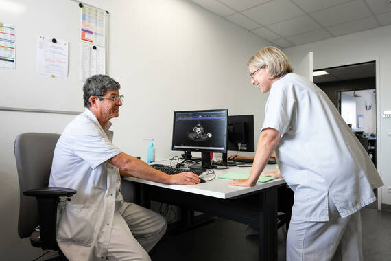 Médecin, assis à son bureau, échange avec une infirmière en pratique avancée dans son bureau. L'ordinateur montre une radiographie. Ils sourient.